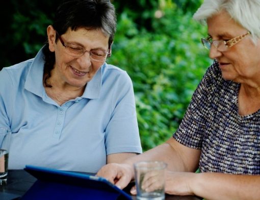Duas idosas sentadas à mesa visualizando algo em um tablet - revisão do benefício
